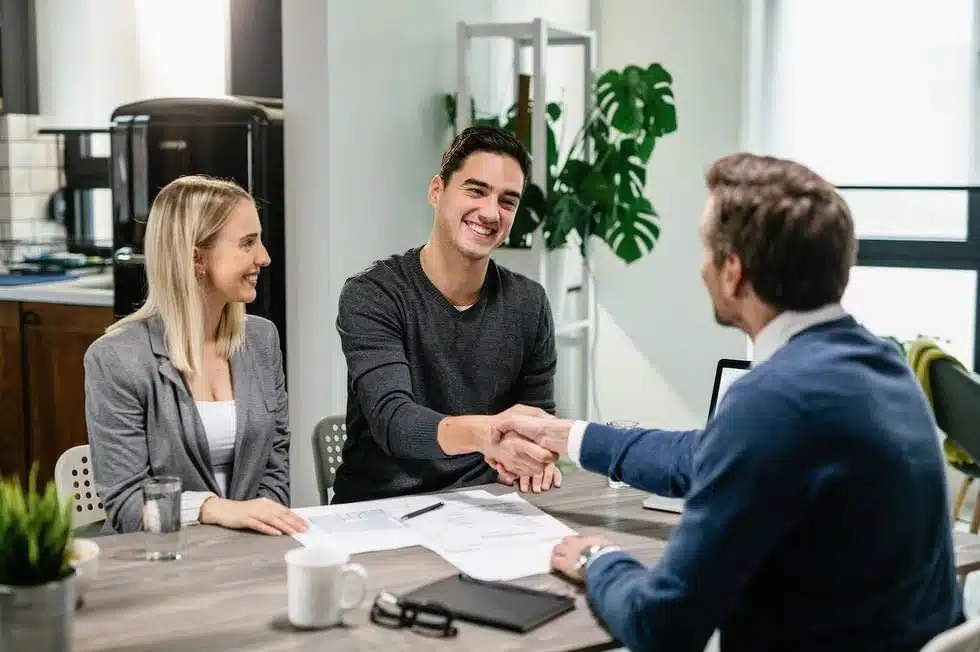 Un jeune couple rencontrant un conseiller en patrimoine pour discuter de leurs investissements.