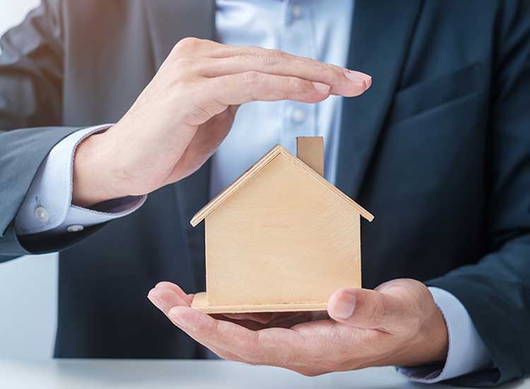 Homme d'affaires protégeant une maison miniature représentant la protection des investissements.