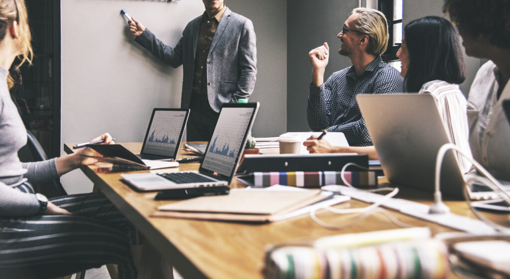 Groupe de personnes en réunion discutant de stratégies d'investissement avec des graphiques et des ordinateurs portables.