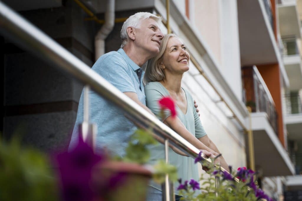 Un couple de personnes âgées se tenant sur un balcon, symbolisant la sérénité et la gestion de patrimoine réussie.